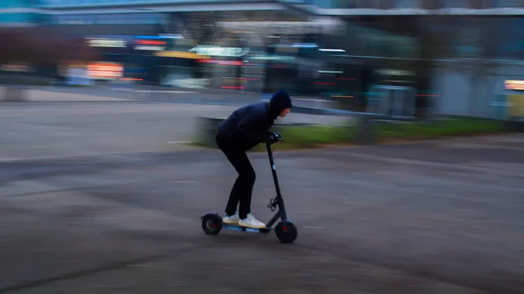 Un homme en veste noire circulant en trottinette électrique dans une rue urbaine.