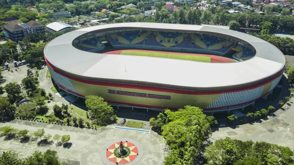 Vue aérienne d'un grand stade moderne entouré d'espaces verts et d'arbres.