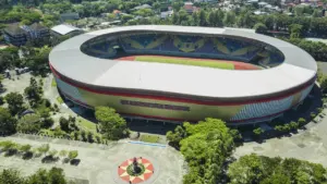 Vue aérienne d'un grand stade moderne entouré d'espaces verts et d'arbres.