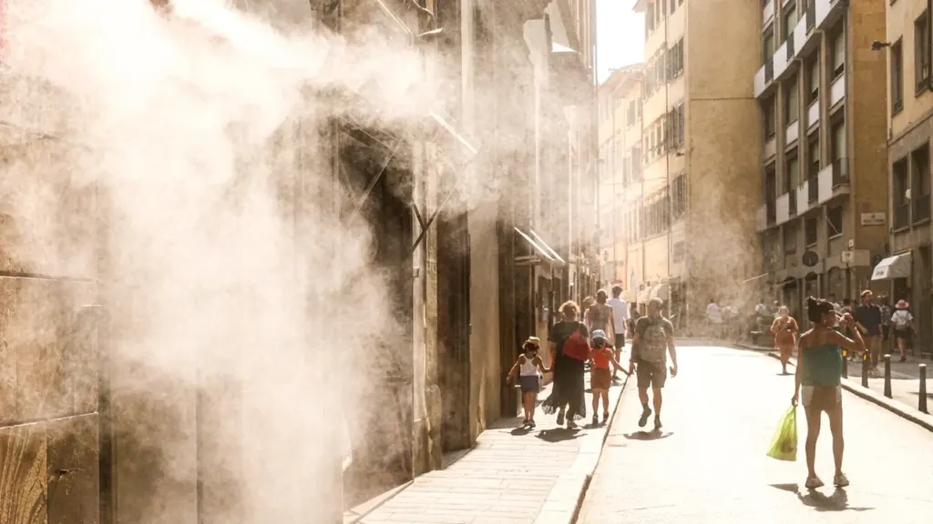 Des piétons marchent sous une brume rafraîchissante dans une rue ensoleillée.