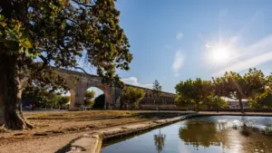 Vaste aqueduc en pierre dominant un bassin d'eau sous un ciel bleu ensoleillé.