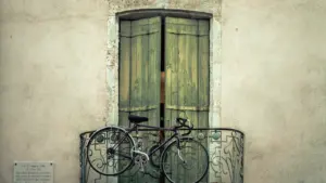 Vieux vélo accroché à un balcon avec volets en bois à Nîmes