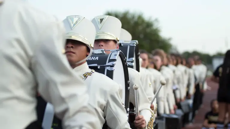Une rangée de jeunes musiciens en uniforme blanc lors d'une parade en extérieur.