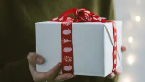 Une personne tenant un cadeau soigneusement emballé avec un ruban rouge festif.
