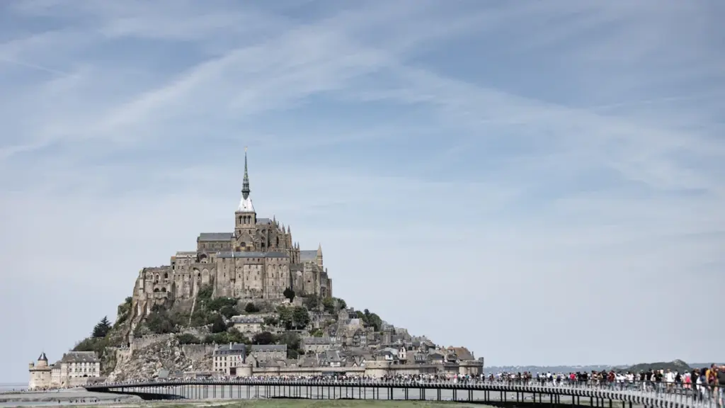Vue panoramique du Mont-Saint-Michel avec des visiteurs sur la passerelle menant à l'abbaye.