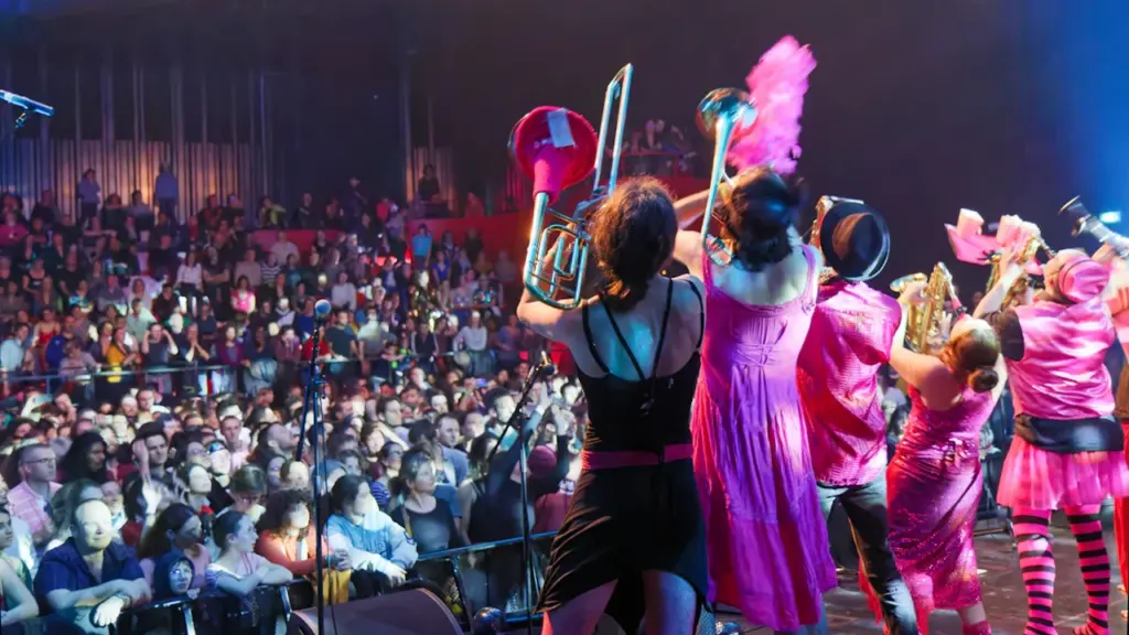 Artistes en costumes roses sur scène devant un public lors d'un concert en plein air.