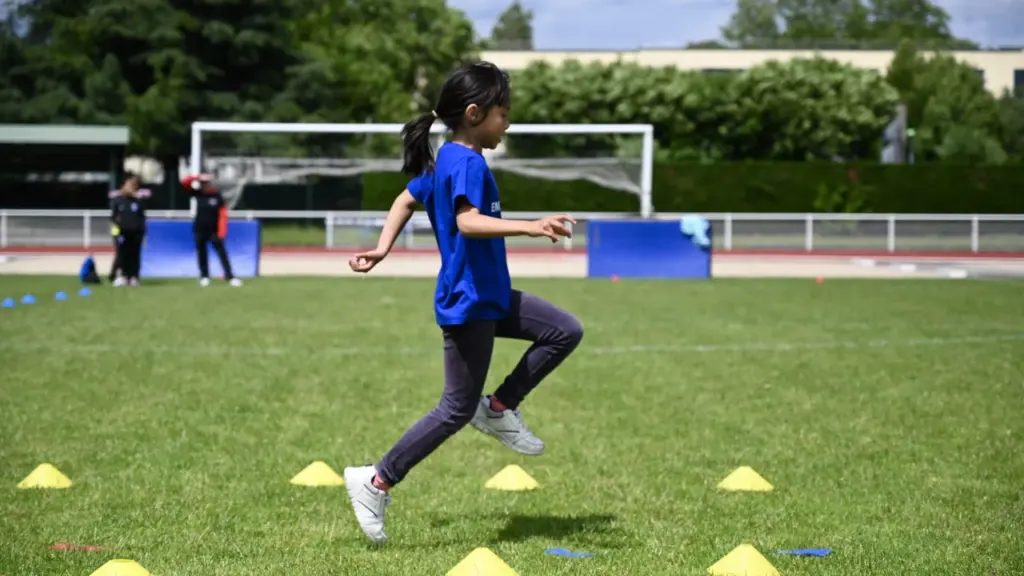 Une jeune fille en t-shirt bleu court sur un terrain de sport herbeux.