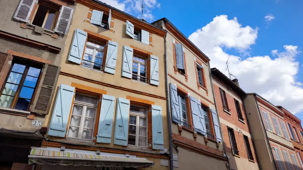 Façades d'immeubles anciens avec volets bleus sous un ciel bleu ensoleillé.