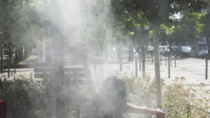 Une personne de dos lève la main dans une fine brume d'eau en extérieur.