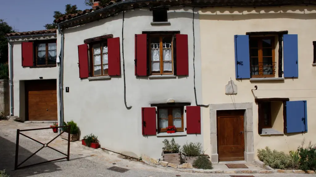 Maison traditionnelle française avec volets rouges et bleus dans une rue pavée.