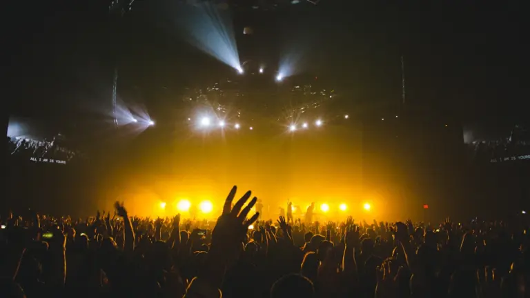 Foule enthousiaste assistant à un concert sous un éclairage scénique doré intense.