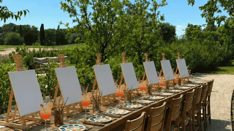 Une longue table en bois en extérieur avec des chevalets et des toiles vierges.