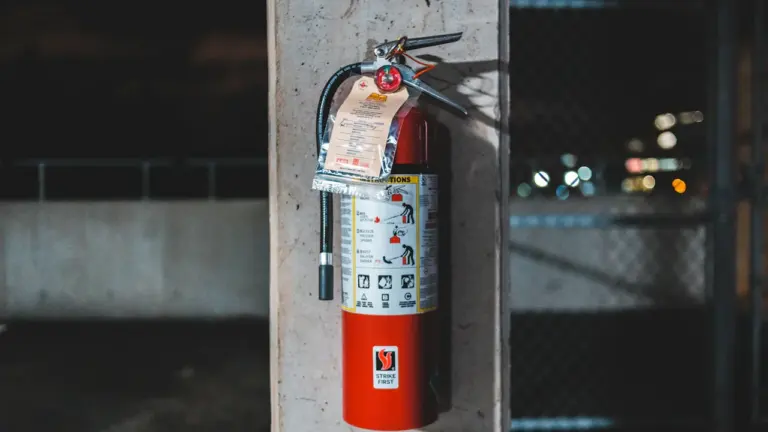 Extincteur rouge monté sur un mur en béton dans un environnement urbain.