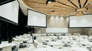 Une salle de conférence moderne avec des tables rondes et des écrans blancs.
