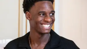 Portrait d'un jeune homme noir souriant, portant une chemise noire et un collier argenté.