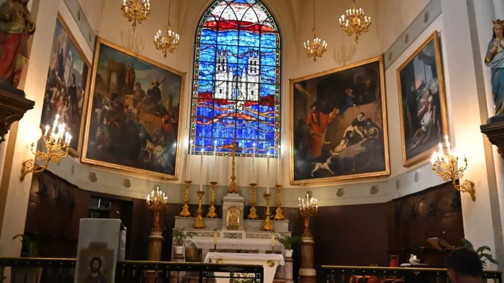 Intérieur d'une église avec des peintures religieuses, un autel et un grand vitrail coloré.