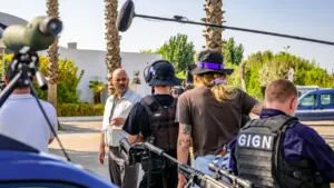 Une équipe de tournage filme un homme en extérieur près d'un agent du GIGN armé.