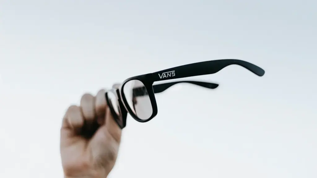 Une main tenant des lunettes de soleil contre un ciel dégagé.