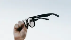Une main tenant des lunettes de soleil contre un ciel dégagé.