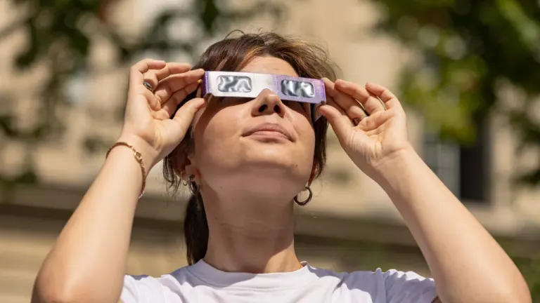 Une jeune femme portant des lunettes de protection spéciales observe une éclipse solaire dehors.