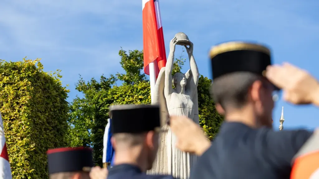 Militaires en uniforme saluant devant une statue de pierre représentant une femme tenant un casque.