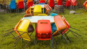 Des chaises colorées empilées sur des tables dans un environnement extérieur verdoyant.