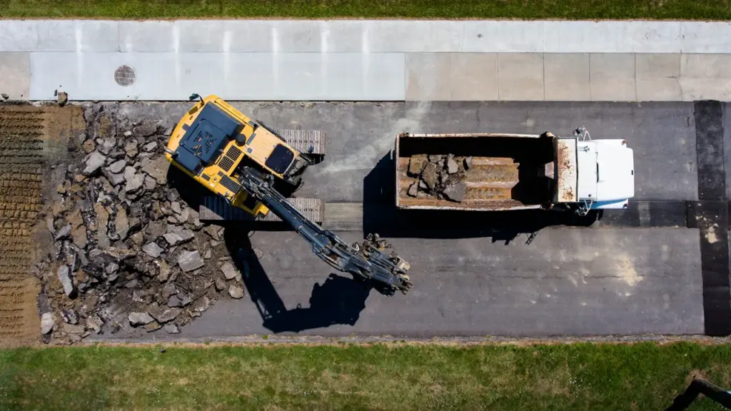 Vue aérienne d'une pelleteuse jaune et d'un camion benne sur un chantier routier.