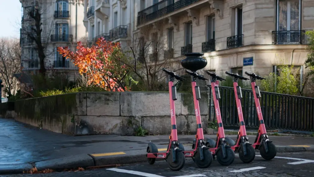 Plusieurs trottinettes électriques rouges garées sur le trottoir dans une rue parisienne.