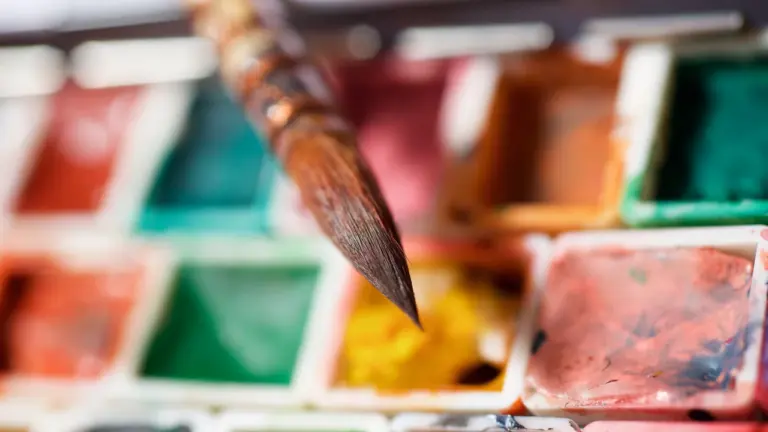 Un pinceau en bois pointu posé au-dessus d'une palette de peintures aquarelles multicolores.