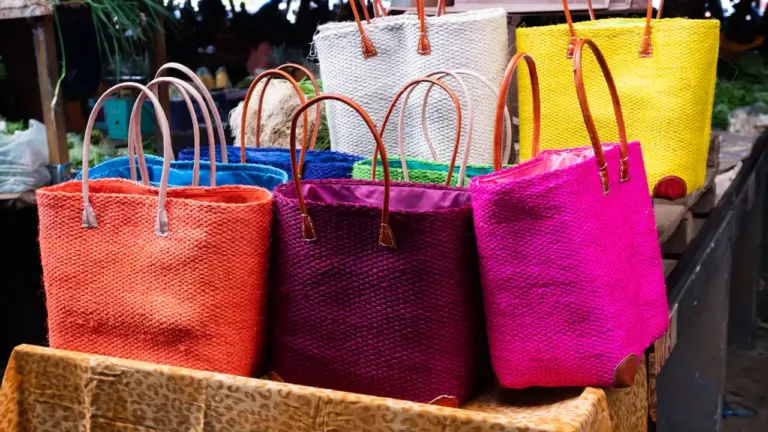 Plusieurs cabas colorés tressés exposés sur une table lors d'un marché en plein air.