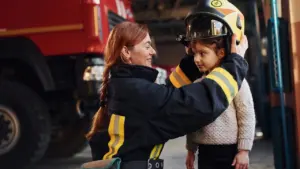Une femme pompier souriante place un casque de protection jaune sur la tête d'une fillette.