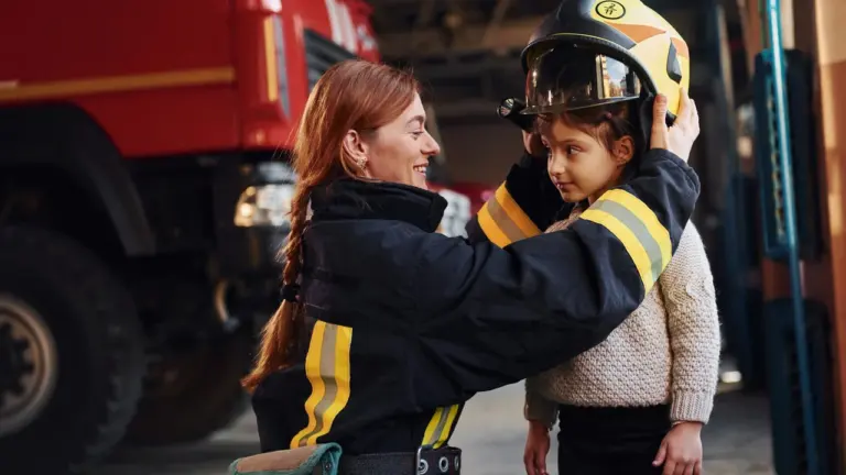 Une femme pompier souriante place un casque de protection jaune sur la tête d'une fillette.
