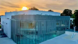 Bâtiment moderne à façade vitrée sous un ciel orangé au moment du coucher du soleil.