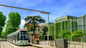 Un tramway blanc décoré de motifs verts s'arrête à une station sous un ciel bleu.