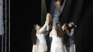 Un groupe de danseurs portant une femme au-dessus de leurs têtes sur une scène sombre.