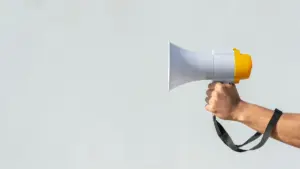 Une main tenant un mégaphone blanc et jaune contre un fond gris clair neutre.