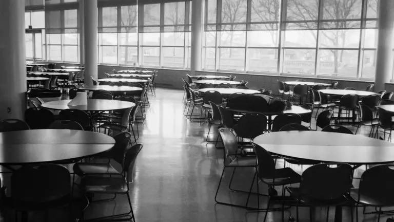 Une cantine scolaire vide avec des tables rondes et des chaises disposées.