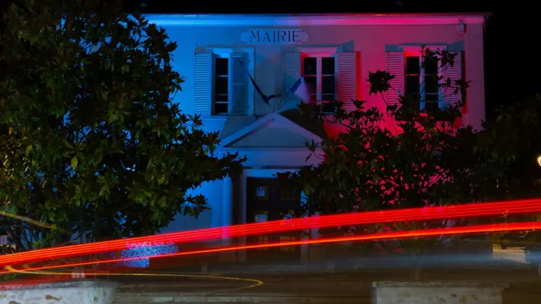 Mairie d'une commune française illuminée aux couleurs bleu, blanc et rouge la nuit.