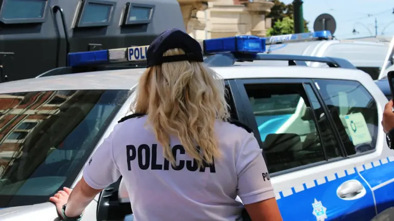 Une policière en uniforme près de son véhicule de service en milieu urbain.