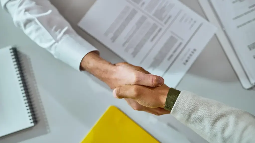 Deux personnes se serrent la main au-dessus d'un bureau avec des documents et dossiers.
