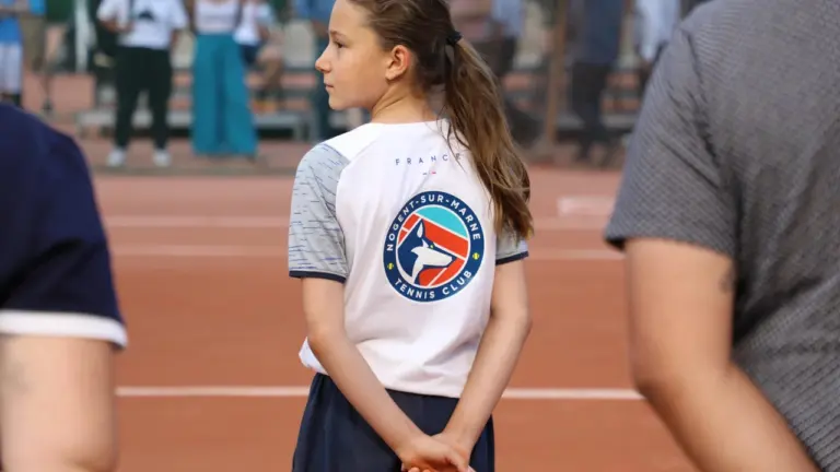 Jeune fille portant un t-shirt blanc du Tennis Club de Nogent-sur-Marne sur un court.