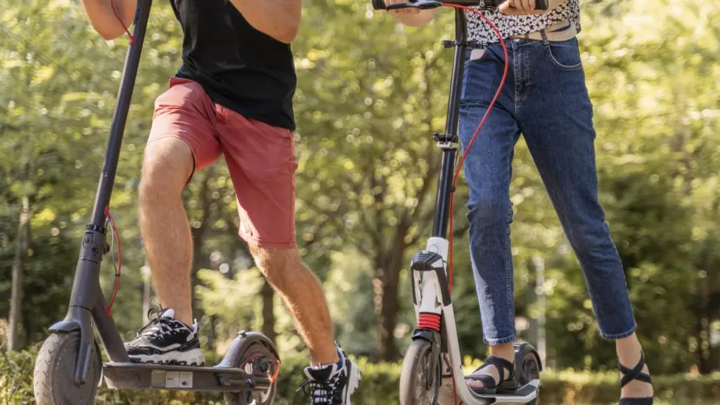 Un homme et une femme conduisent des trottinettes électriques sur un chemin pavé ensoleillé.