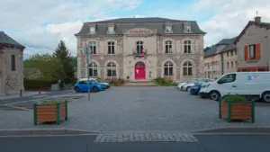 Bâtiment de la mairie avec des voitures garées devant sur une place pavée.