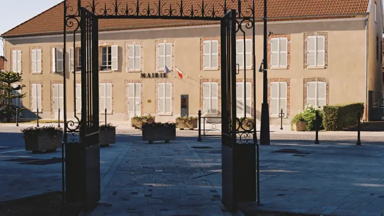 Vue de face d'une mairie française classique avec son portail en fer forgé ouvert.