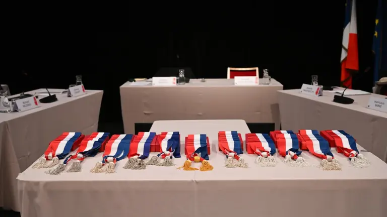 Plusieurs écharpes tricolores françaises sont disposées sur une table devant des sièges d'élus.